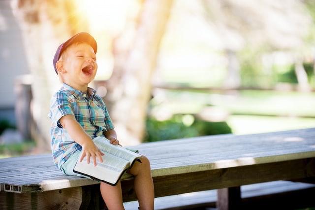 Child laughing with Bible, pray like a three year old