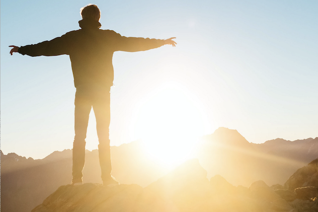 man on mountain looking at sunrise, being born again