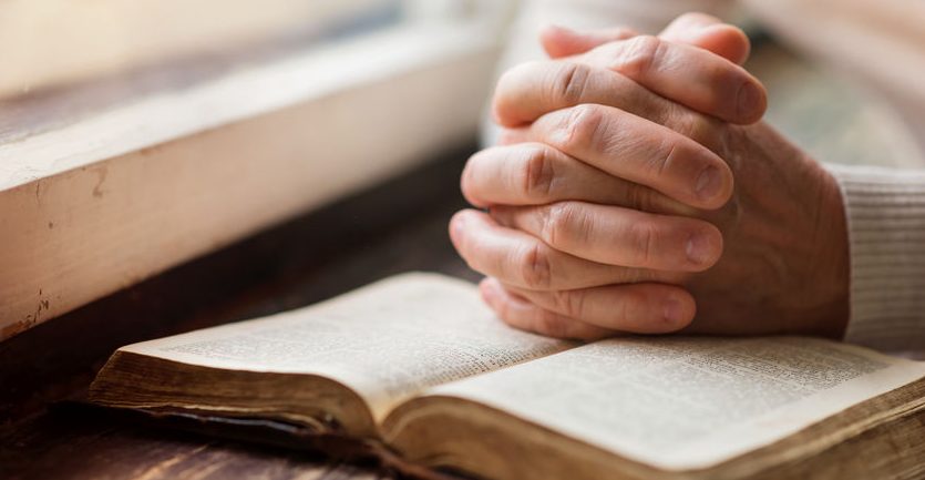 hands praying on a Bible, how to find yourself in the Bible